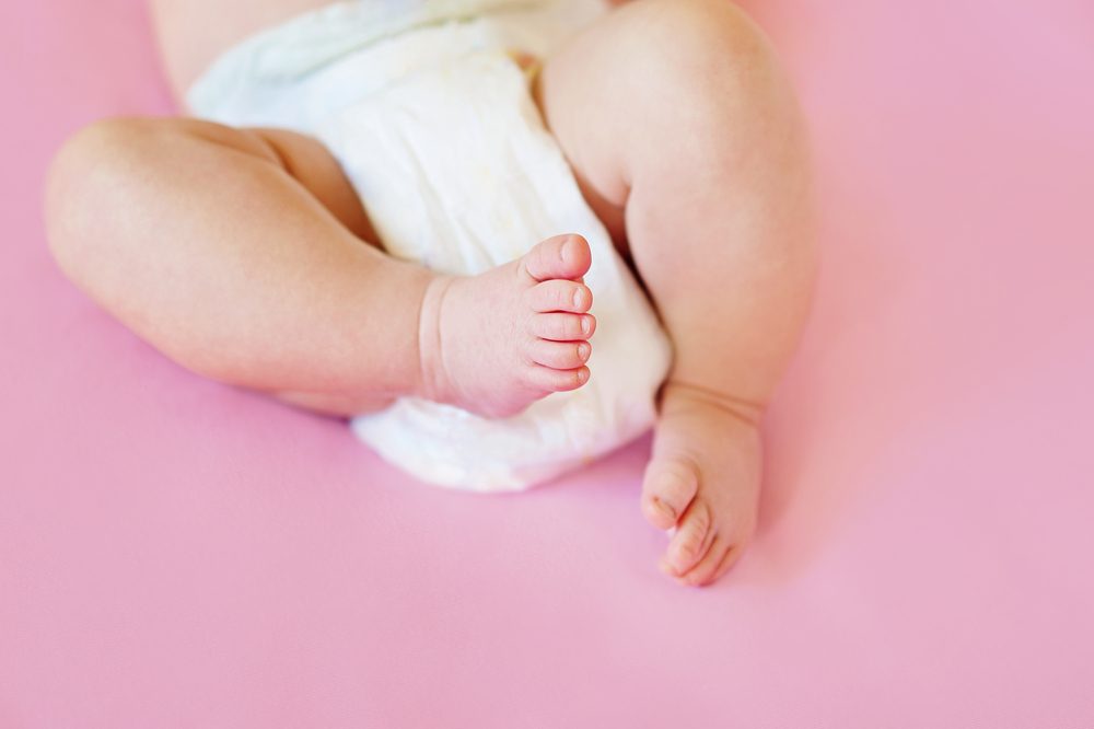 feet of a two months old baby wearing diapers lying on the bed at home